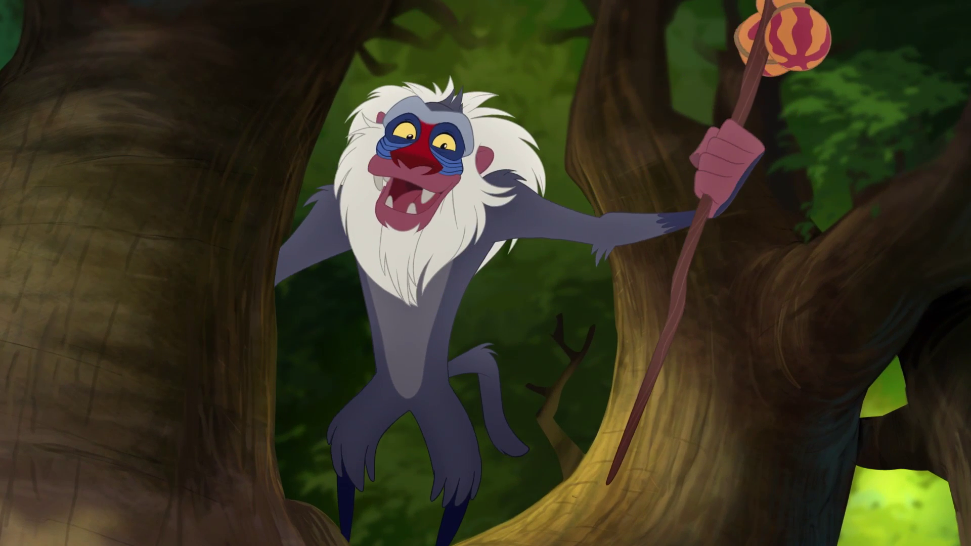 Rafiki from The Lion Guard smiles and looks down as he stands in a tree with his cane in one hand.