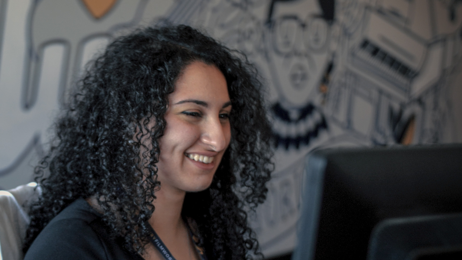 An animator from Mercury Filmworks works on her computer with a unique wall mural behind her.