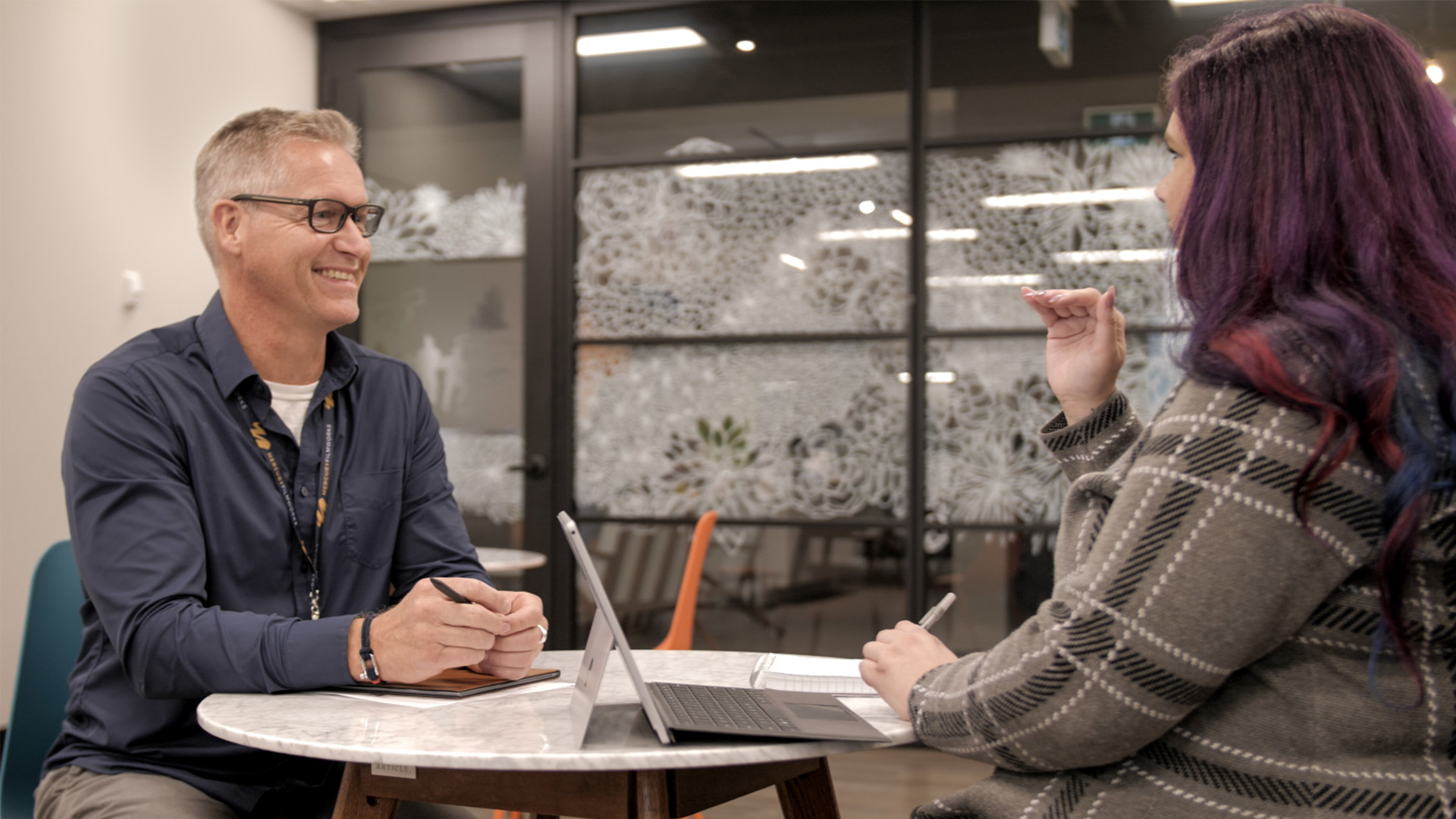 Two employees from Mercury Filmworks sit and talk at a table together as David smiles.